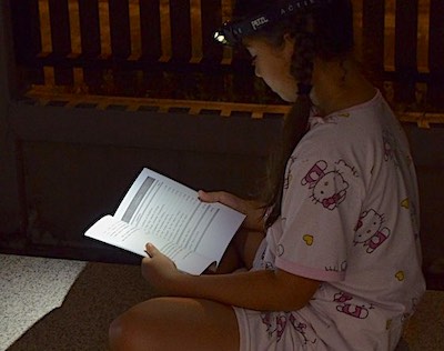 Girl reading a book at night with a headlamp.